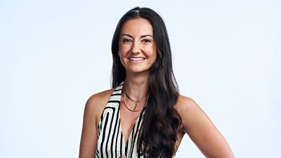 A woman with long dark hair, wearing a black and white striped sleeveless top, smiles to camera