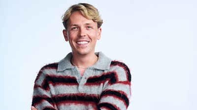 A man in a grey and red striped fluffy polo shirt smiles to camera