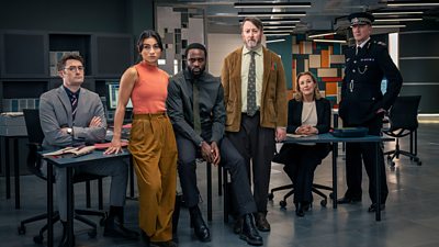 Group image. The cast of Ludwig series two stand in an office, featuring DS Ethan Cole (BEN ASHENDEN); DC Caitlin Sullivan (RUMI SUTTON); DI Russell Carter (DIPO OLA); John ‘Ludwig’ Taylor (DAVID MITCHELL); DCS Carol Shaw (DOROTHY ATKINSON); and Chief Constable Ziegler (RALPH INESON).
