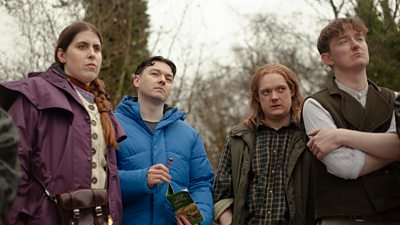 Four people stand outdoors and watch something offscreen. One holds a leaflet for an activity.