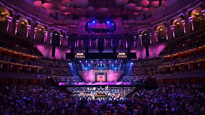 The royal albert hall with an orchestra in the middle surrounded by a crowd. Purple lights are spread across the room