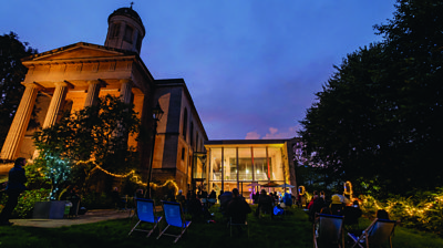 A photo of St George's in Bristol, with a group of people sitting on loungers on a grass area in front of the theatre