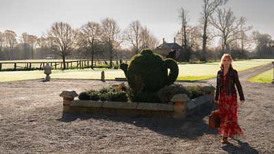 Lesley Manville as Susan Ryeland. She walks up the long gravel driveway of a grand property. 