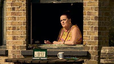 A women wearing bright clothing sits against a window ledge looking into the distance