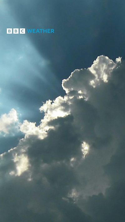 Large white cloud stretching across a blue sky with rays of sunshine