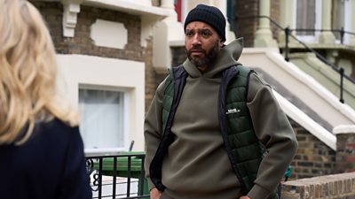 Samuel Anderson in character as Mal. Standing outside a house, he looks concerned as he speaks with someone offscreen. 