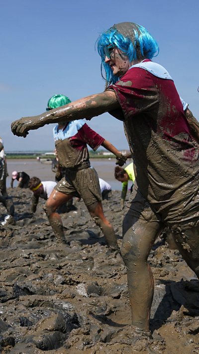 Woman wear a red top and blue wig and she marches through mud flats during the Maldon Mud Race