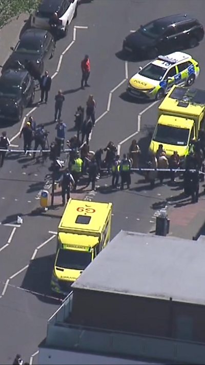 Two ambulances and a police car seen surrounded by about a dozen people