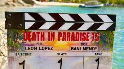 Clapperboard for Death in Paradise series 16 on the shoreline on location in the French Caribbean. 