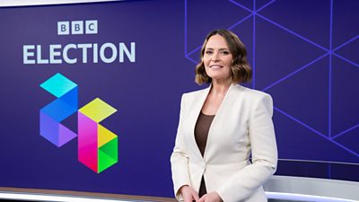 Laura Miller wearing a white jacket standing in front of the words BBC Election 26
