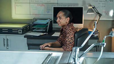 A woman sits behind a desk in a laboratory