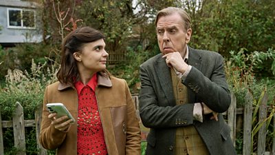 Gwyneth Keyworth and Timothy Spall in character looking at each other. Behind them is a residential garden