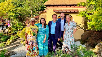 Five people stood in a bright garden smiling towards camera
