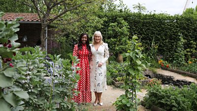 Angellica Bell and Nicki Chapman wearing dresses stood in a pristine garden smiling at the camera