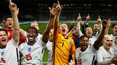 A group of football players wearing England shirts celebrating and pointing to the sky