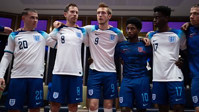 A group of football players lined up for a team talk before a game. They are wearing a white England kit with their arms around each other