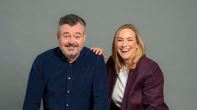Grant Stott and Arlene Stuart sat in front of a grey background smiling towards the camera