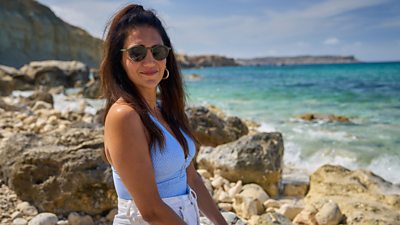 Η Leila Farzad στον χαρακτήρα ως Nat. Φορώντας γυαλιά ηλίου, χαμογελά και κοιτάζει κατευθείαν στην κάμερα. Είναι καθισμένη σε βράχια δίπλα στη θάλασσα. 