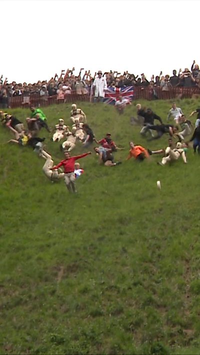 People chasing a wheel of cheese down a hill.