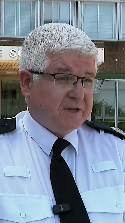 A head and shoulders shot of a police officer in a white shirt and glasses. He has a small mic clipped onto his tie.