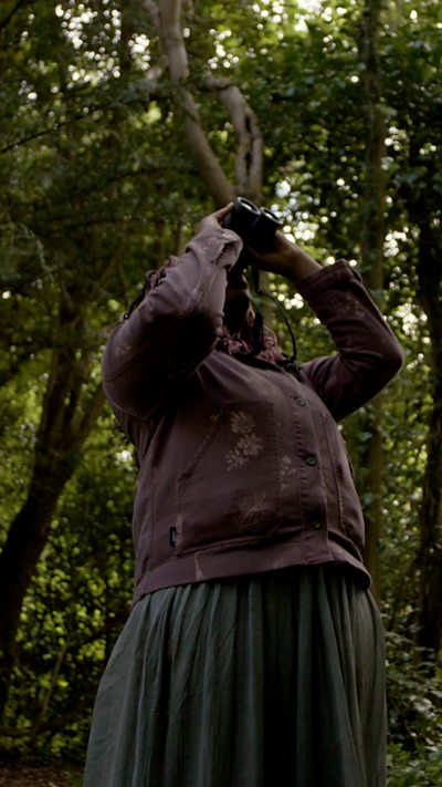 Environmentalist, Dominique Palmer, looks through binoculars in the woods