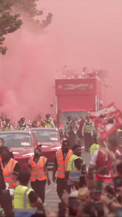 Sky turns red with Arsenal fan's flares as people and cars fill the street.