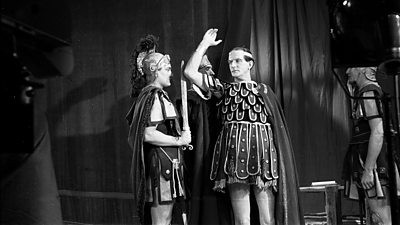 Two actors appear in period costume during a TV production of Julius Ceasar.