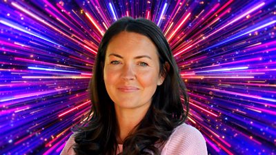 A woman with long dark hair smiles to camera, set against a glittering background with rays of red, pink, purple and blue light