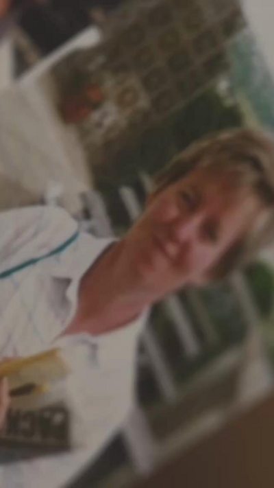Blurred and old photo of a woman wearing a white shirt and holding a newspaper. She has dark blonde hair.