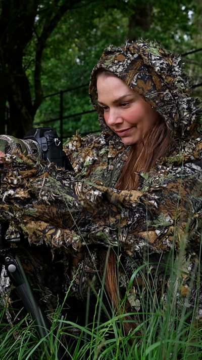 Hannah Stitfall looks at the back of her camera while in camo gear in a field
