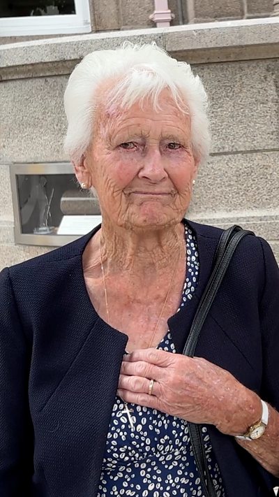An elderly woman smiles with tears in her eyes outside Jersey's parliament