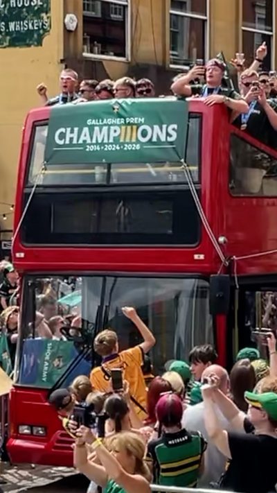 A large red double decker bus surrounded by crowds with people dressed in Saints kits on the open roof