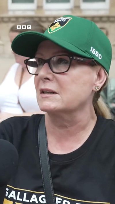 A woman is speaking to a microphone while wearing a Saints cap