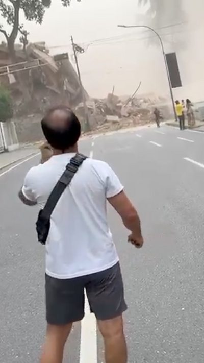 A man stands on a street staring towards a collapsed building.