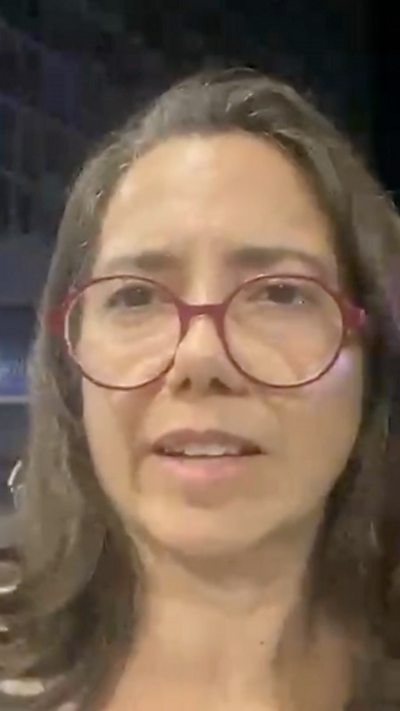 A woman with grey hair and red glasses looks into the camera.