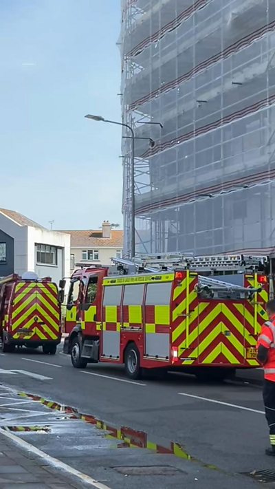 Two fire engines beside a tall building which is covered in sheeted scaffolding