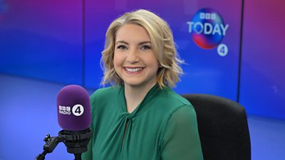 Today Programme presenter, Anna Foster, sits in a studio chair in front of purple Radio 4 Today branding with a microphone. She has blonde, shoulder length hair and a green blouse.