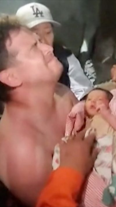 Man holding a baby wrapped in a pink blanket.