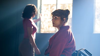 Two women in a dark misty room as a light beams in from dusty windows