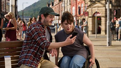 A man showing his phone to a woman in a town centre square on a hot summers day