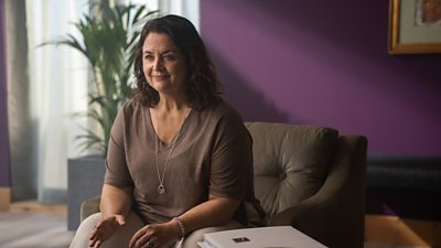 A woman sat in a purple room sat next to a box of files