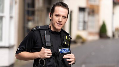 Ben Castle-Gibb as a policeman smiling into camera