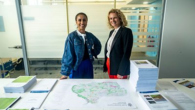 Anita Rani reports from South Tyneside Council. She stands in a denim jacket smiling, next to MP Anna Dixon, who wears red trousers and a black blazer. They stand over a map of the region.