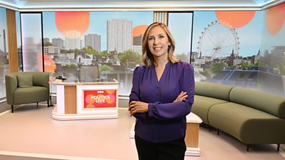 Presenter Vicki Young in the new Politics Live studio. Vicki has blonde hair and a purple shirt. The background shows a green sofa and chair set up with Politics Live branding and a London landscape projected behind.