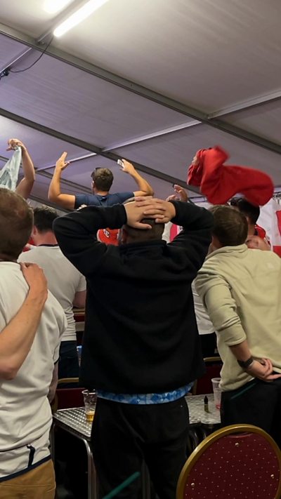 People watching a football game in a crowd with their head in their hands.