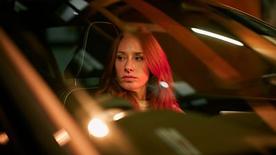 Professor Hannah Fry sits in the front seat of a car, looking out the window.