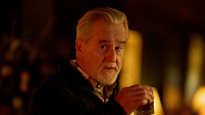 A man with grey hair and a goatee looks away from camera with a drink in his hand