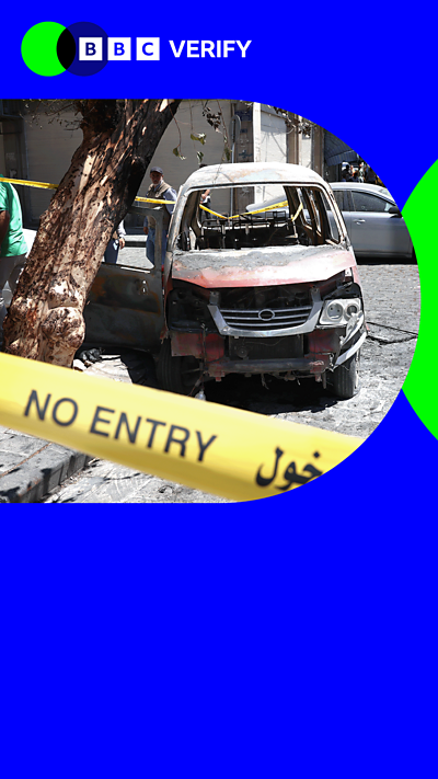 A burned out car behind 'no entry' yellow tape in a blue border.