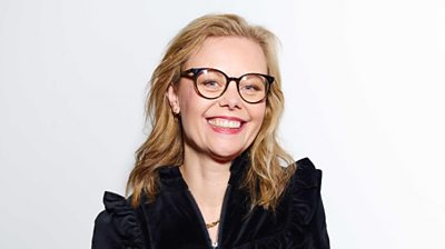 A blonde woman wearing dark rimmed glasses and a black shirt smiling at the camera.