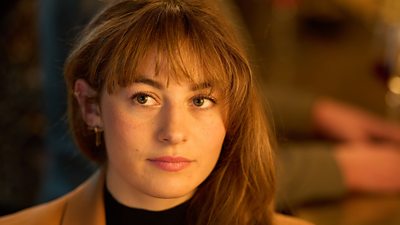 A young woman is pictured in close up, looking at someone off screen. Her hair is tucked behind one ear.